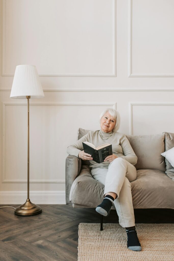 Elderly woman enjoying a book while sitting on a comfortable sofa at home.